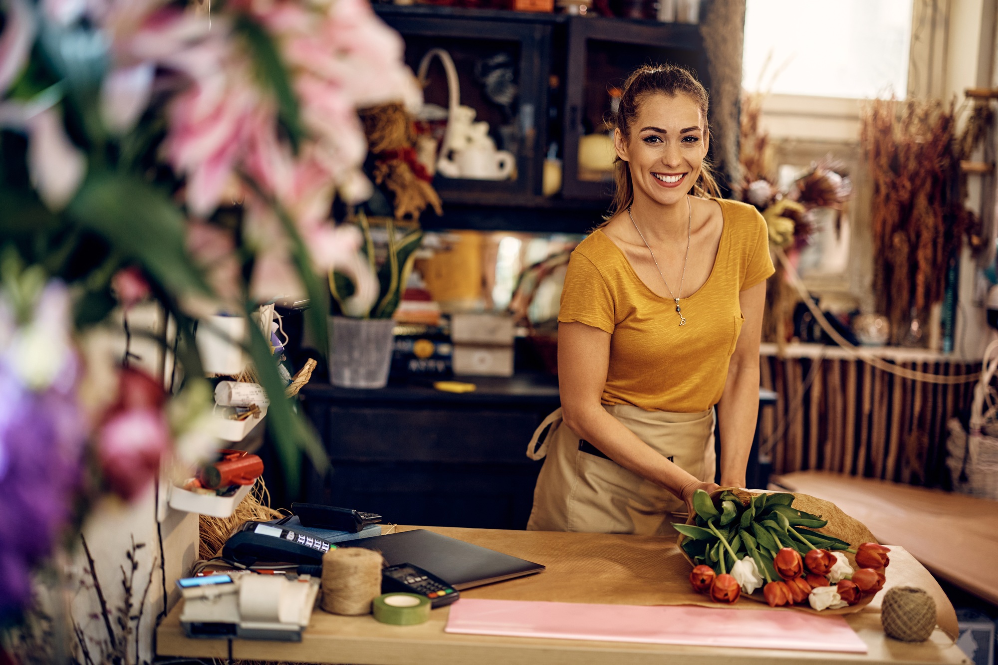 Happy female flower shop owner making bouquet of tulips and looking at camera.
